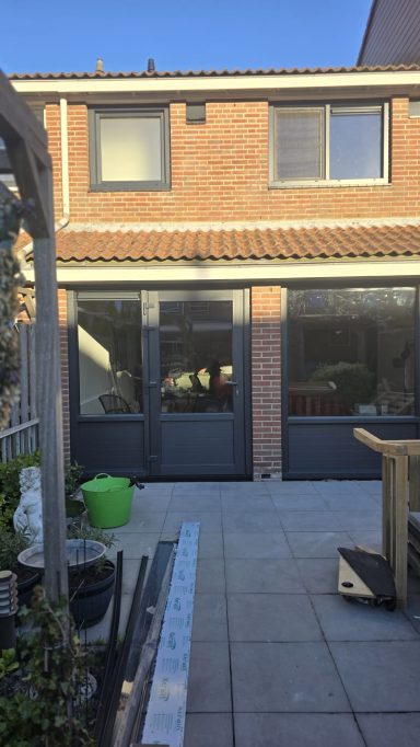 Een moderne achtertuin met een betegeld terras en een garage met grote deuren.